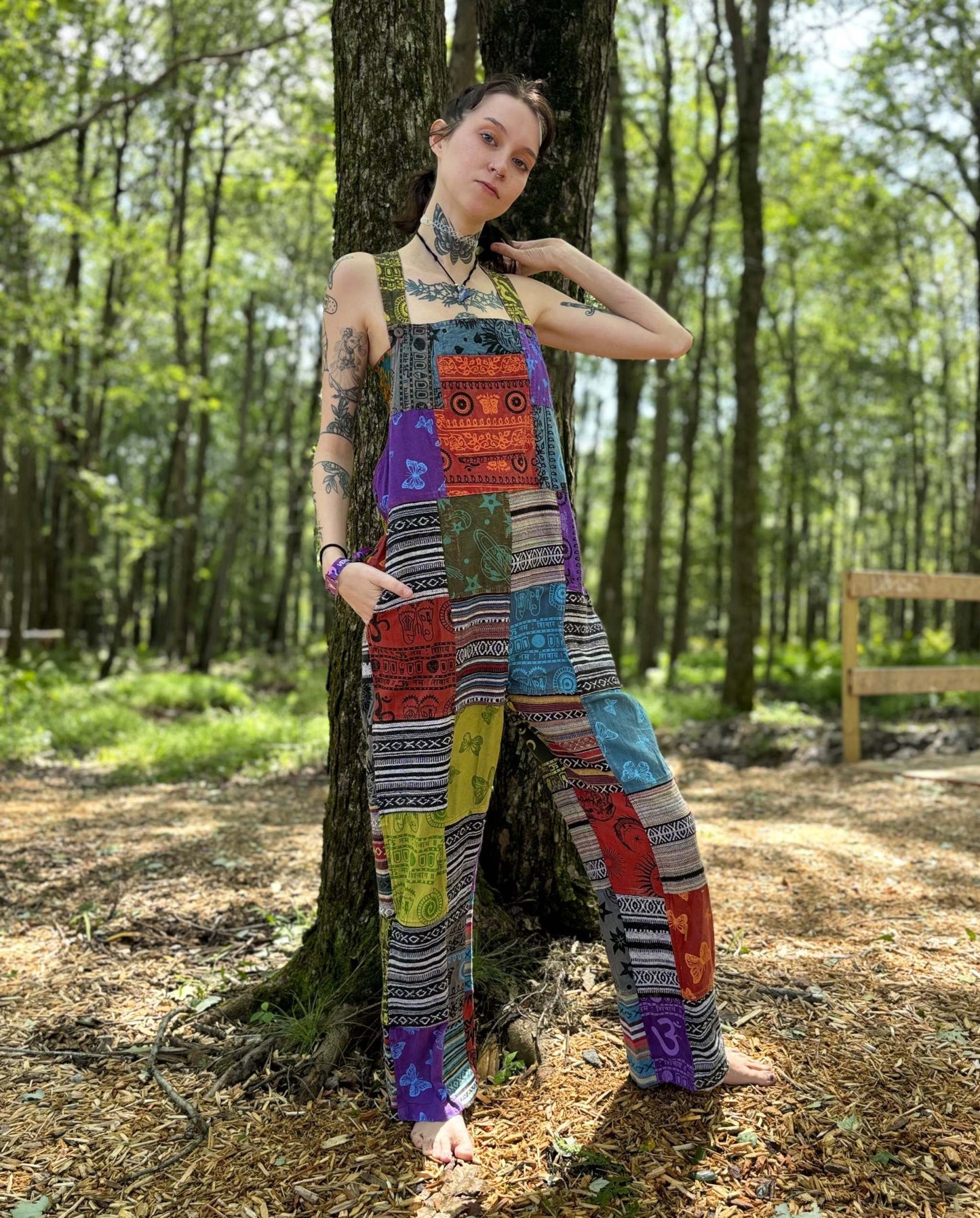 Multicolor ikat patchwork overalls with adjustable straps in a forest setting.