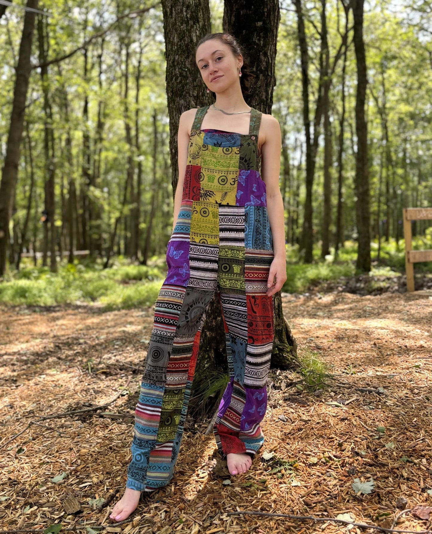 Multi color Ikat patchwork overalls with adjustable straps in a forest setting.
