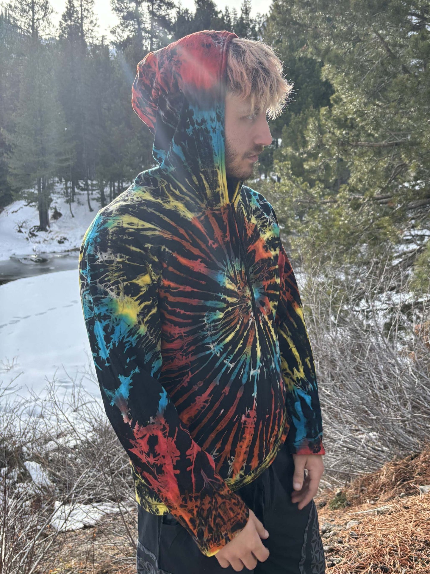 Man wearing a light tie-dye hoodie with vibrant colors in a snowy forest.