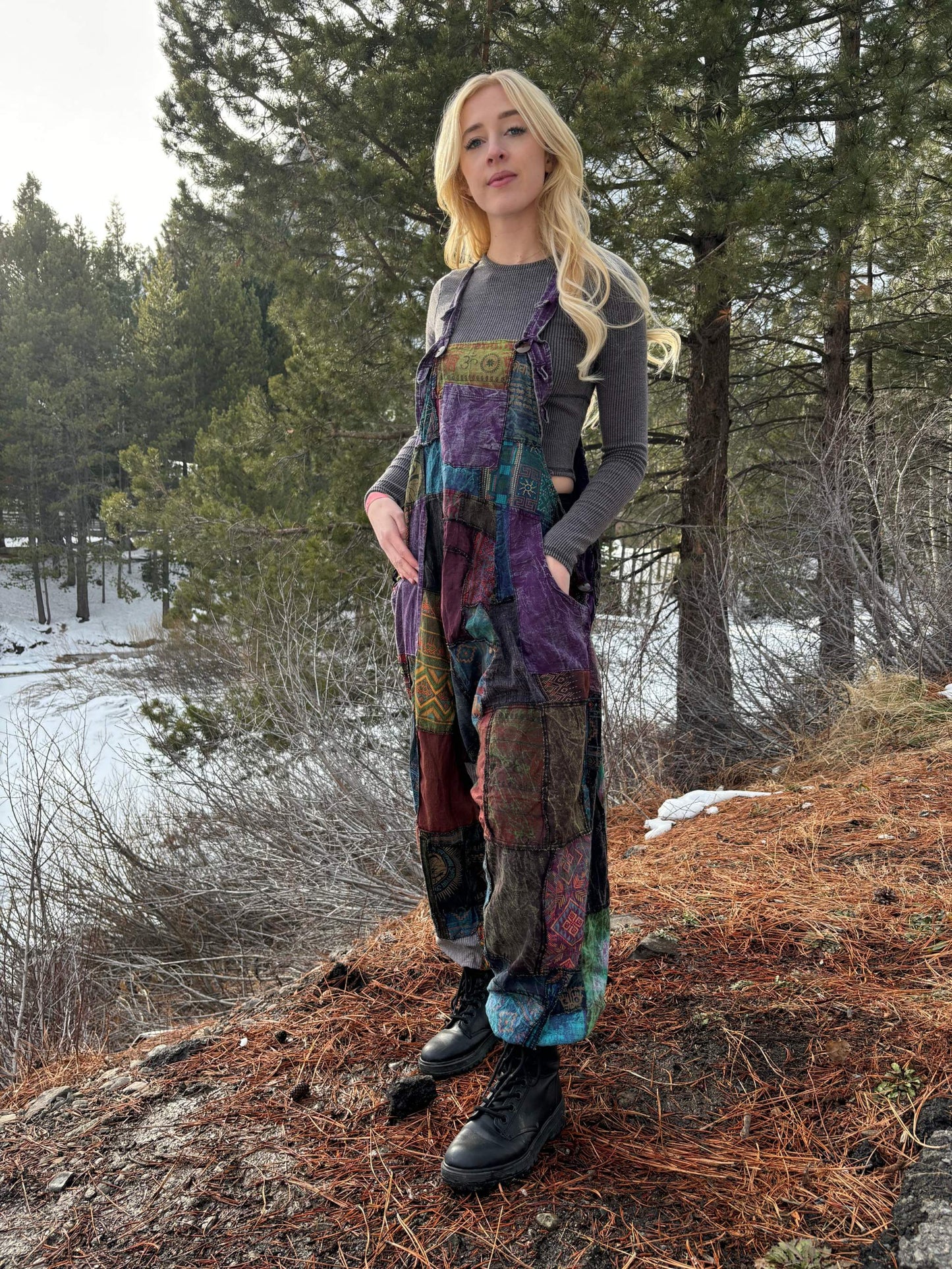 Woman wearing patchwork harem overalls outdoors with forest background.