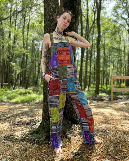 Multicolor ikat patchwork overalls with adjustable straps in a forest setting.