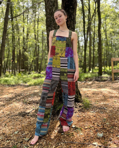Multi color Ikat patchwork overalls with adjustable straps in a forest setting.