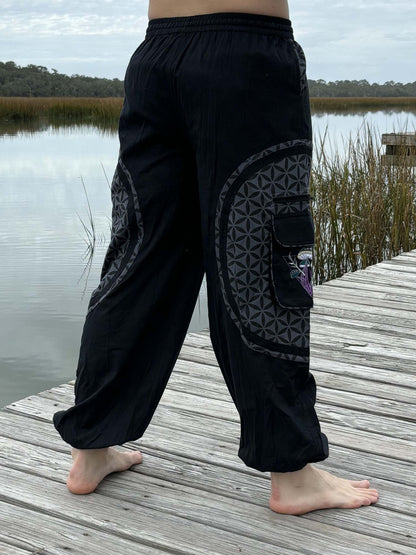 Hippie Mushroom Harem Pants with embroidery and pockets, black color, handmade cotton fabric, worn by person on wooden dock.