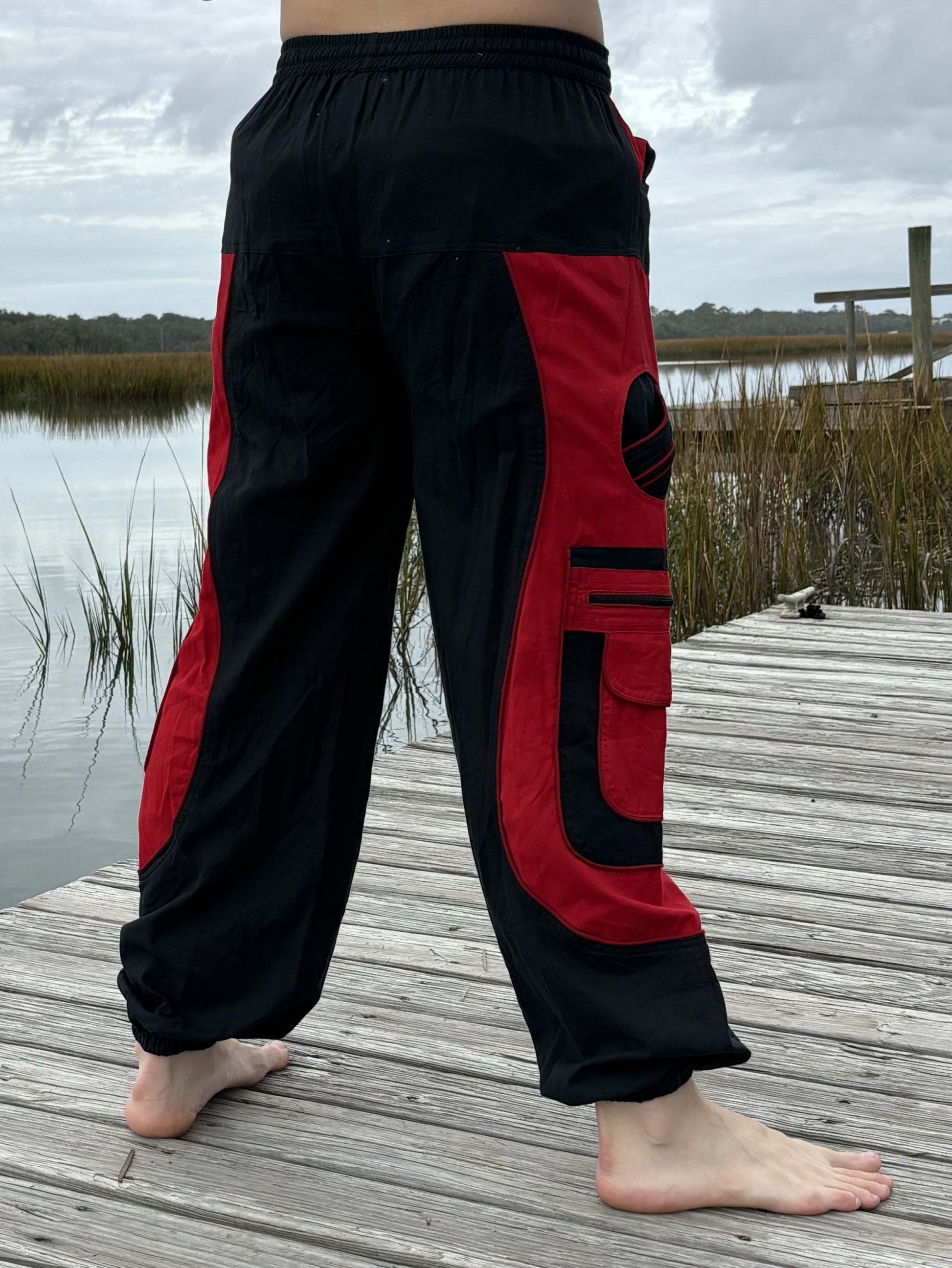 9 pocket harem pants with red and black design, elastic waist and cuffs, on a wooden dock near water.