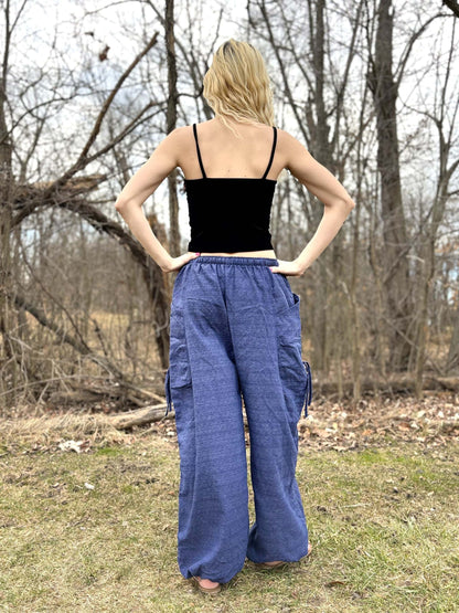 Woman wearing blue cinch leg harem pants with elastic waist and ankle cuffs in a forest setting.